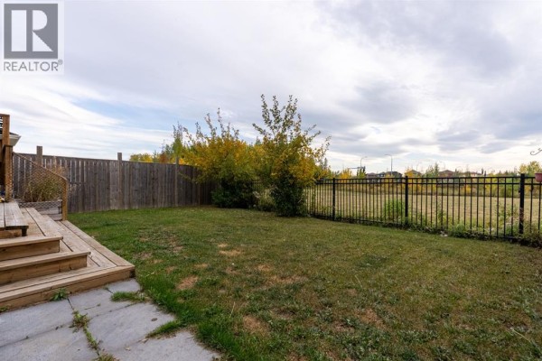 Backyard with wooden fence, green grass, and a view of the distant neighborhood. - 209 Blackburn Drive, Fort Mcmurray