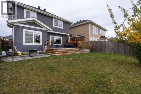 Side view of the backyard of a dark grey house with a wooden deck and trees. - 209 Blackburn Drive, Fort Mcmurray