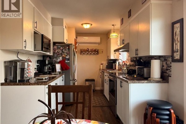 Narrow galley kitchen with white cabinets, granite countertops, stainless steel appliances, and a small dining nook. - 209 Centennial Heights Street, Dalhousie