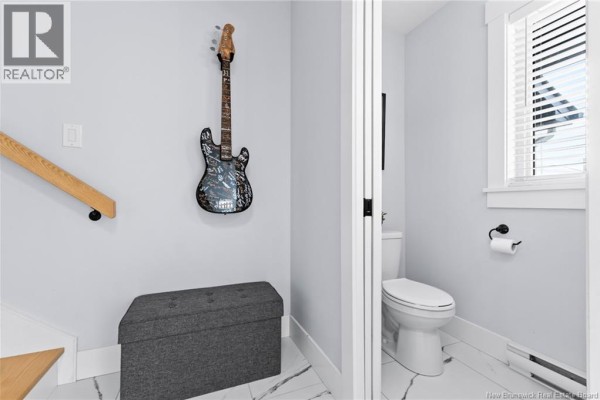 Close-up of a small bathroom with white toilet, window, and light blue walls. - 209 Norbert Street, Dieppe
