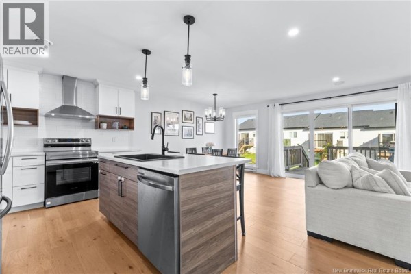 Modern kitchen with white cabinets, gray island, stainless steel appliances, and open dining area. - 209 Norbert Street, Dieppe