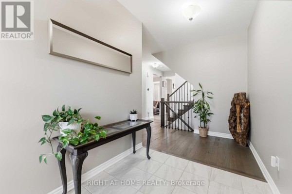 Foyer with gray walls, dark wood floors, a console table with plants, and a staircase. - 209 Quarter Horse Street, Ottawa