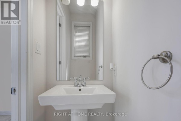 Powder room with a white pedestal sink, chrome faucet, and a silver towel ring. - 209 Rivertree Street, Ottawa