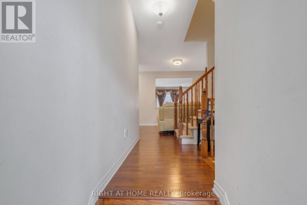 Hallway with hardwood floors leading to a staircase with wooden banisters. - 209 Rivertree Street, Ottawa