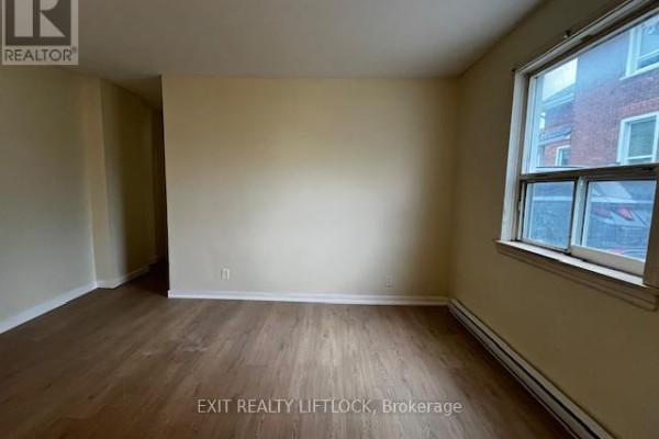 Living room with beige walls, wood laminate flooring, and a large window overlooking the street. - 209 Stewart Street, Peterborough