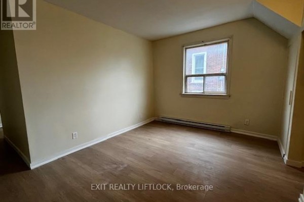 Bedroom with beige walls, wood laminate flooring, a small window, and a baseboard heater. - 209 Stewart Street, Peterborough