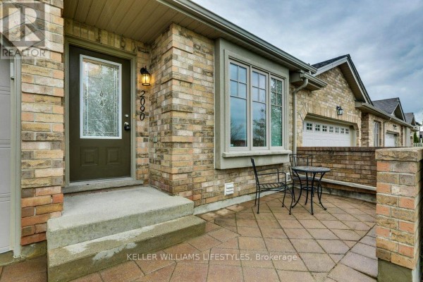 Close-up of the townhouse entrance with a brown door, beige brick, and a small patio. - 2090 Denview Avenue, London North