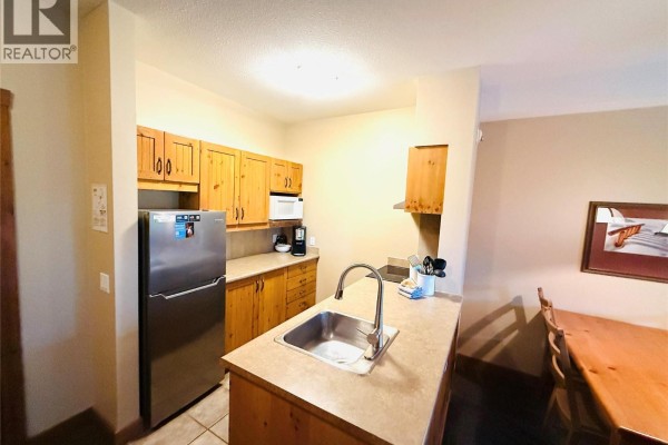 Kitchen area with sink, refrigerator, wooden cabinets, and microwave. - 2090 Summit Drive Unit# 106, Panorama
