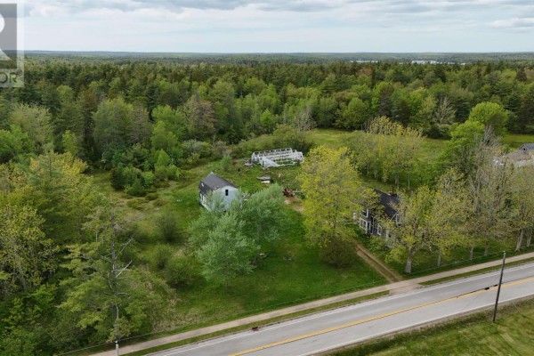 Side view of a two-story dark blue house with a front porch and shingle siding, surrounded by grass and trees. - 2091 Highway 203, Kemptville