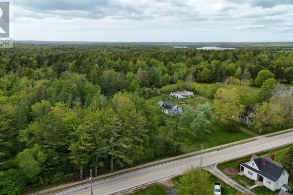 Aerial view of a residential property with two houses, a greenhouse, and extensive woodland bordering a paved road. - 2091 Highway 203, Kemptville