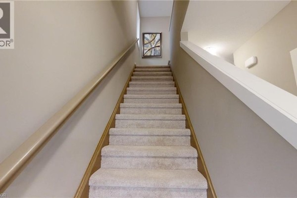 Carpeted staircase with a wooden handrail leading upwards between neutral-colored walls. - 2092 Evans Boulevard, London