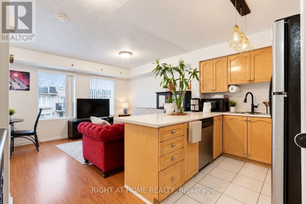 Open-concept living and kitchen area with wood floors, light wood cabinets, and red sofa. - 2095 - 55 George Appleton Way, Toronto