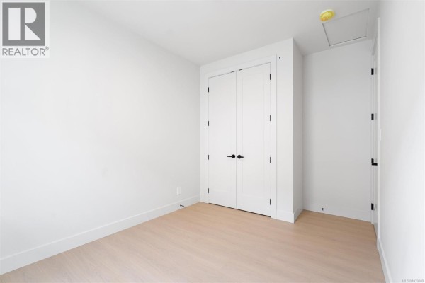 Empty room with white walls, light wood floors, and a double door closet. - 2098 Kingbird Dr, Langford
