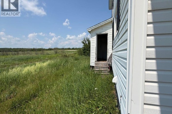 Side view of a white house showing a narrow entrance door and tall grass. - 2099-2101 Champlain Street, Dieppe