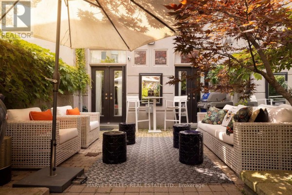 Outdoor patio seating area with white wicker sofas, dark stools, and a large umbrella. - 21 - 260 Russell Hill Road, Toronto