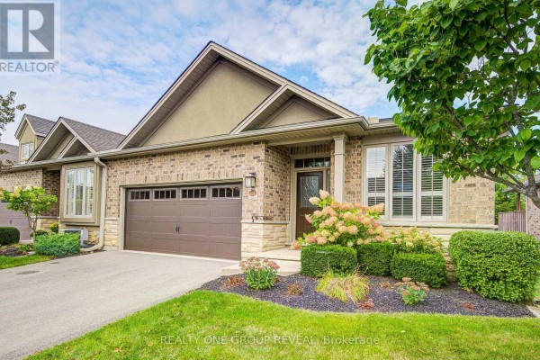 Side view of a brick townhouse with a garage, manicured landscaping, and a large tree. - 21 - 30 Cedar Street, Brant