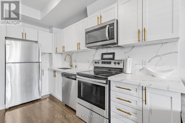Close-up of a modern kitchen with white cabinets, stainless steel appliances, and gold hardware. - 21 - 630 Rogers Road, Toronto