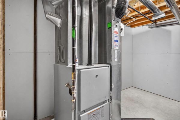 Close-up of a large grey furnace and metal ductwork in a room with concrete floor. - #21 15151 43 St Nw Nw, Edmonton