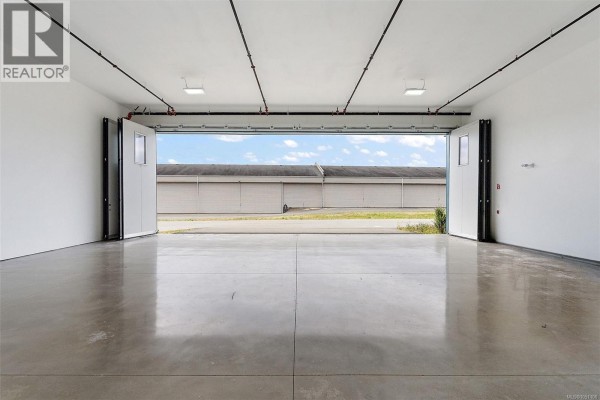 A wide shot of an empty airplane hangar with large bi-fold doors open to an exterior view. - 21 1663 Mills Rd, North Saanich