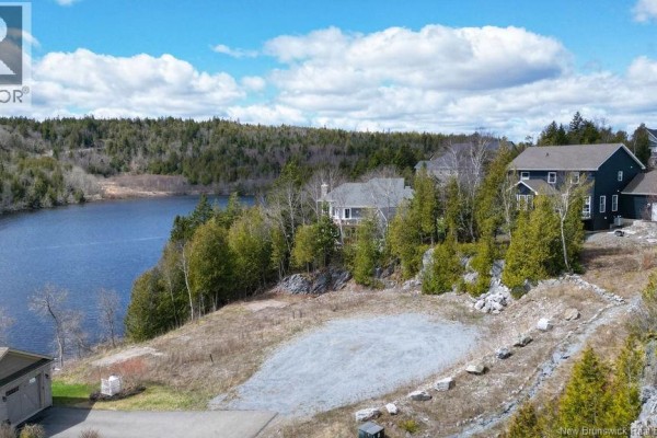 View of cleared waterfront lot with gravel base, surrounded by trees and neighboring houses. - 21-2 Upper Deck Lane, Saint John
