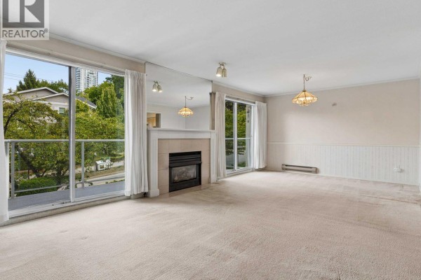 Living room with beige carpet, fireplace, mirrored wall, and large windows. - 21 5575 Patterson Avenue, Burnaby