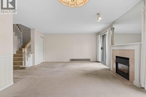 Living room with beige carpet, fireplace, staircase, and sliding glass door. - 21 5575 Patterson Avenue, Burnaby