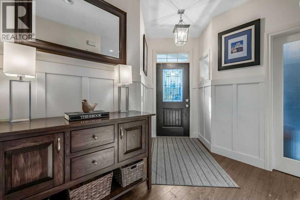 Foyer with dark wood flooring, white wainscoting, and a dark front door with a stained-glass insert. - 21 Ascot Crescent Sw, Calgary
