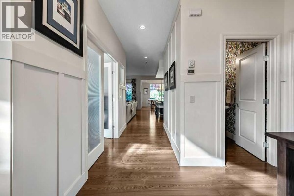 Interior hallway with hardwood floors, white wainscoting, and doorways to different rooms. - 21 Ascot Crescent Sw, Calgary