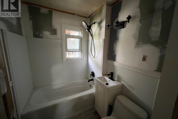 A bathroom with a white bathtub, small white vanity, toilet, and unfinished walls. - 21 First Avenue, Kingston