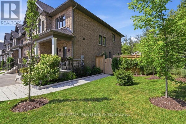 Side exterior of a brick townhouse with a green lawn, paved walkway, and wooden fence. - 21 Gord Matthews Way, Uxbridge