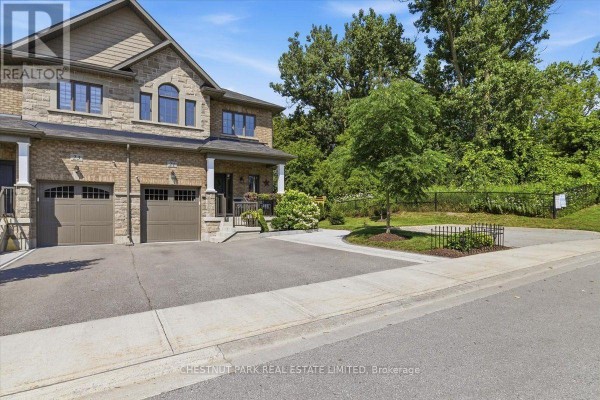 Street view of townhouse exteriors with paved driveways and surrounding trees. - 21 Gord Matthews Way, Uxbridge