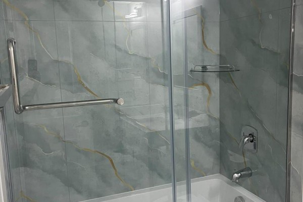 Close-up of a bathtub with a glass shower door and light green marble-patterned tiles. - 21 Hartford Trail, Brampton