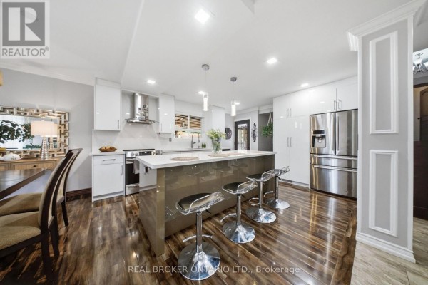 View of the modern kitchen with stainless steel appliances, island, and pendant lights. - 21 Kendleton Drive, Toronto