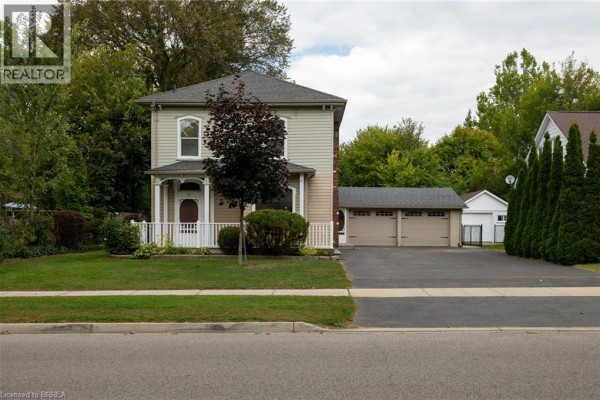 Front view of a two-story beige house with a white picket fence and mature trees. - 21 Mccall Street, Simcoe