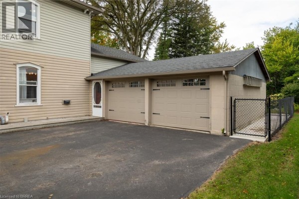 Tan three-car garage attached to the house with a chain-link fence on the side. - 21 Mccall Street, Simcoe