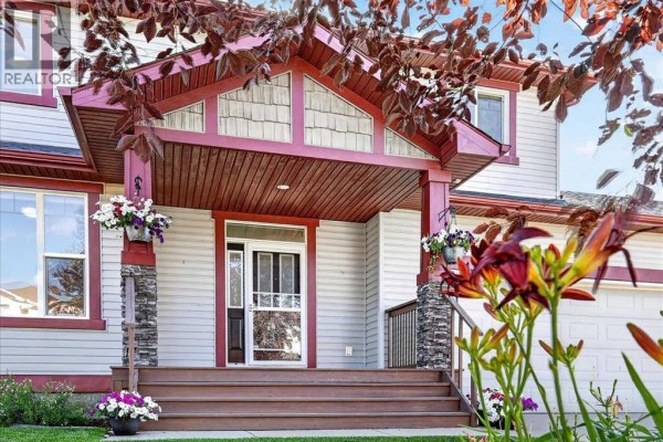 View of the covered entryway with decorative beams, stone pillars, and flowering plants. - 21 Mcintyre Place Nw, Langdon