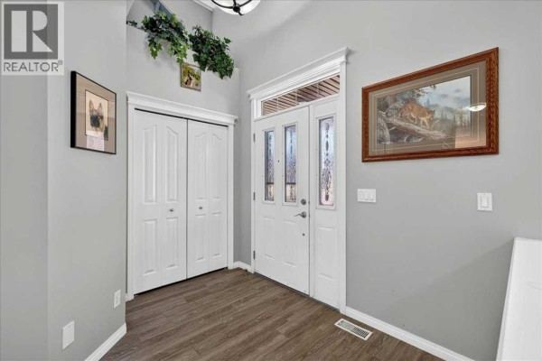 Interior entryway with grey walls, white double doors, a white front door with glass panels, and wood-look flooring. - 21 Mcintyre Place Nw, Langdon