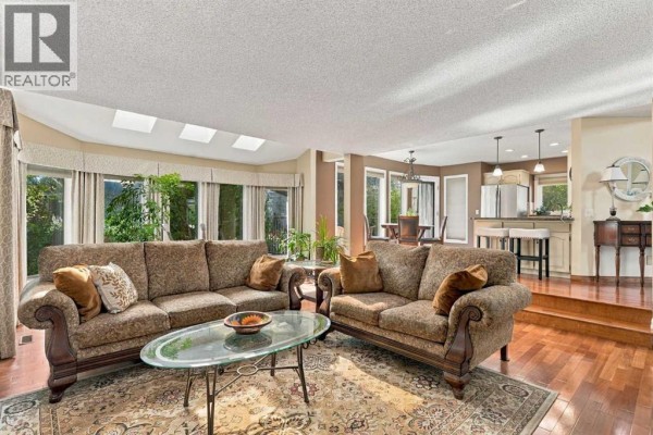 Living room with plush patterned sofas, glass coffee table, hardwood floors, and a view of greenery through large windows. - 21 Mt Robson Close Se, Calgary