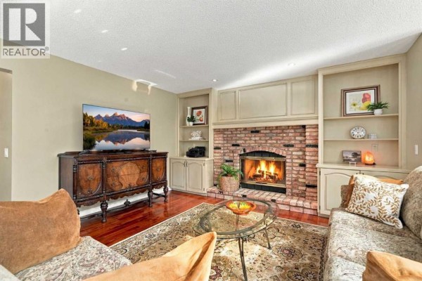 Living room with a brick fireplace, built-in shelving, a television on an antique stand, and plush seating. - 21 Mt Robson Close Se, Calgary