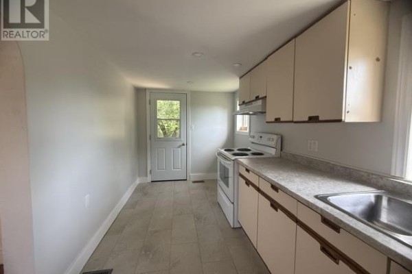 Kitchen with white cabinets, gray tile floor, white stove, and a door leading outside. - 21 Park St, Thessalon