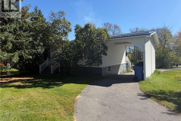 Side view of a white house with trees, a driveway, and a carport. - 21 Second Street, Miramichi