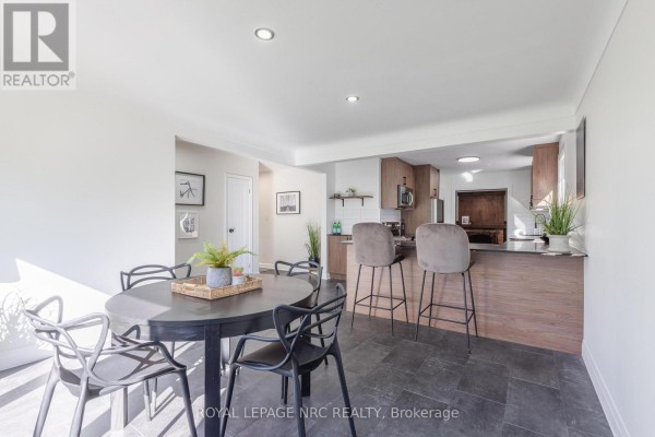 Interior dining area with a dark round table, black chairs, and a large window. - 21 Silverdale Drive, St  Catharines