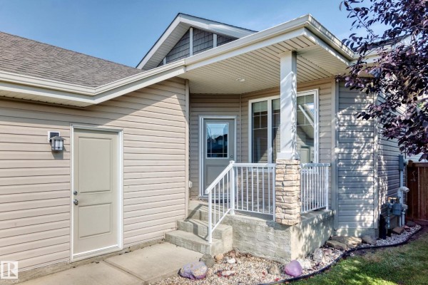 Exterior view of the house entrance with beige siding, stone pillar, and landscaping. - 21 Silverstone Dr Nw, Stony Plain