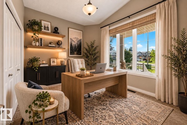A home office with a wooden desk, armchair, shelved wall, and large window with a street view. - 21 Silverstone Dr Nw, Stony Plain