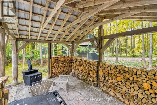 Outdoor covered area with stacked firewood, a black wood stove, and two chairs. - 21 Slalom Drive, Oro Medonte