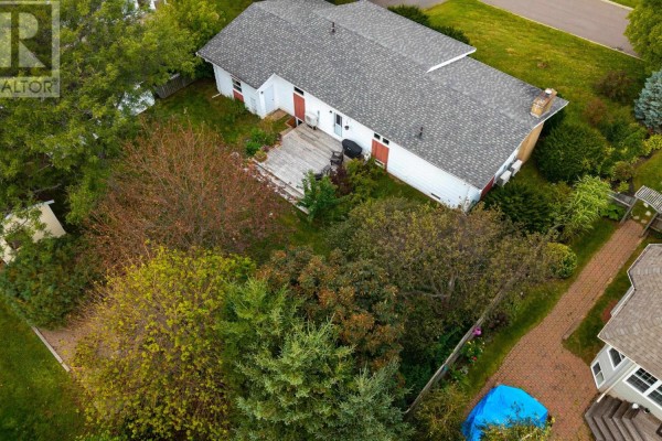 Aerial view of the backyard of a white house, showing a wooden deck and surrounding trees and shrubs. - 21 Smallwood Crescent, Charlottetown