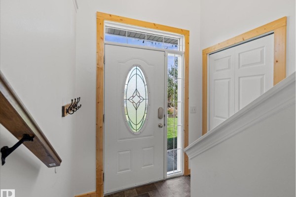 Interior view of the front entrance with a white door, wood trim, and a coat rack. - 21 Spruce Meadow Ln, Bon Accord