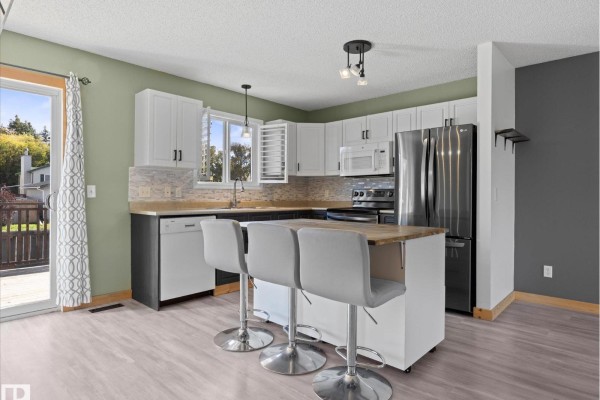 Kitchen with white upper cabinets, dark lower cabinets, stainless steel appliances, and island with stools. - 21 Spruce Meadow Ln, Bon Accord