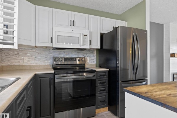 Close-up of the kitchen's stainless steel appliances, stove, and dark grey cabinets. - 21 Spruce Meadow Ln, Bon Accord