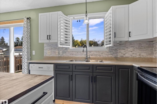 Kitchen sink with double basin, window with shutters, dishwasher, and view of the backyard. - 21 Spruce Meadow Ln, Bon Accord
